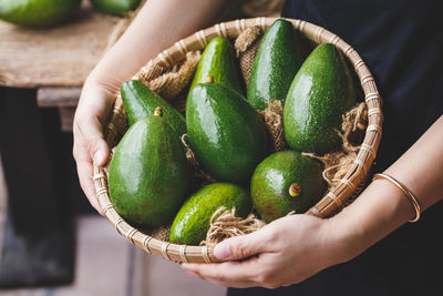 Midsection of woman holding avocadoes in basket