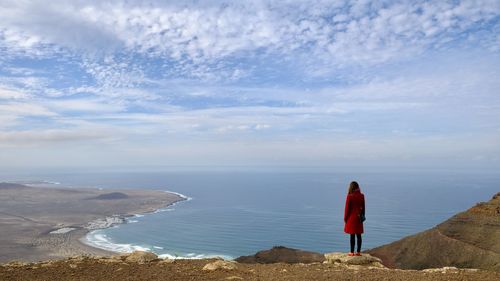 Rear view of woman standing on cliff against sea and sky