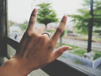 Cropped hand of woman showing horn sign by window glass