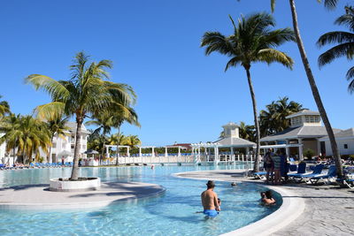 People relaxing by swimming pool against clear blue sky