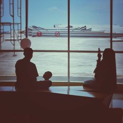 Rear view of silhouette man sitting by window