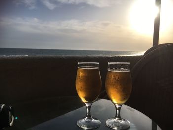 Close-up of beer on table at beach against sky during sunset