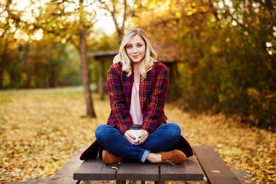 Portrait of young woman sitting in park during autumn