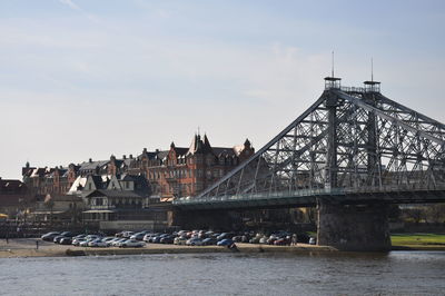 Bridge over river by buildings in city against sky