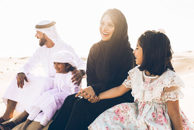 Arabian family sitting at desert against sky