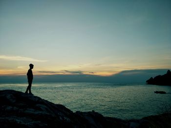 Silhouette man looking at sea against sky during sunset