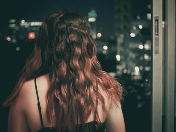 Rear view of woman against window in home at night