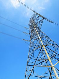 Low angle view of electricity pylon against blue sky