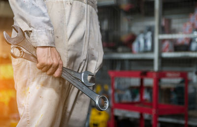 Midsection of mechanic holding spanners in garage
