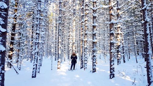 Woman standing on snow covered field amidst trees