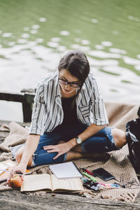 High angle view of woman studying while sitting on pier against lake in forest