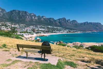 People on bench by sea against clear blue sky