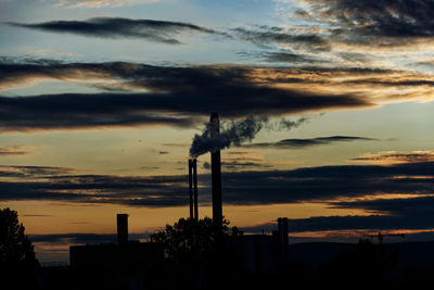 Silhouette of smoke stacks against sky during sunset