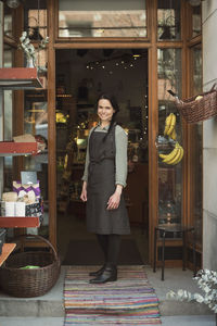 Full length portrait of smiling owner standing at store entrance