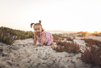 Portrait of baby girl crawling on sand at beach against clear sky