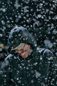 Happy man wearing warm clothing while standing during snowfall at night