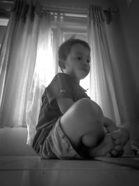 Girl looking away while sitting on window at home