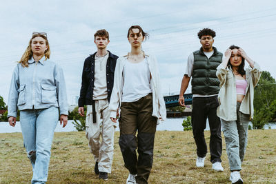 Full length portrait of confident young friends walking against sky