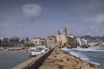 Buildings by sea against cloudy sky