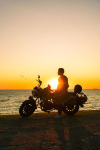 Rear view of man riding bicycle on beach against sky during sunset