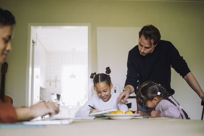 Father homeschooling daughters sitting at dining table