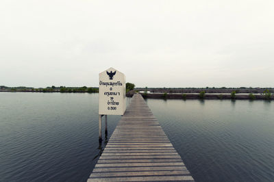 Sign by wooden jetty over lake against cloudy sky