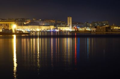 Illuminated buildings by river against sky at night