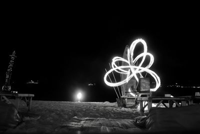 People at illuminated amusement park against sky at night