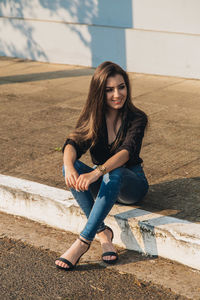 High angle view of smiling young woman sitting on footpath