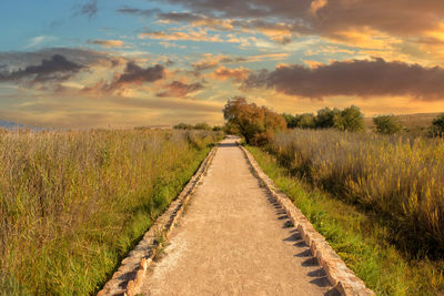 Road amidst field against sky during sunset