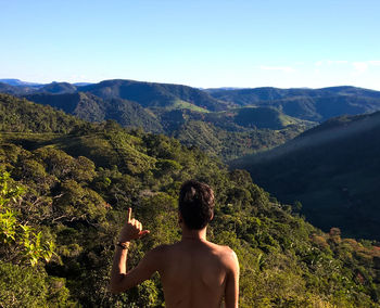 Rear view of shirtless man gesturing shaka sign against mountains