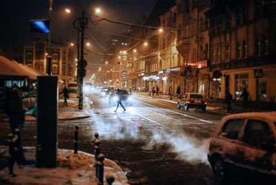 People and cars on illuminated city street at night