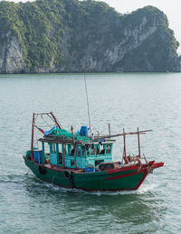 Fishing boats sailing in sea against mountains