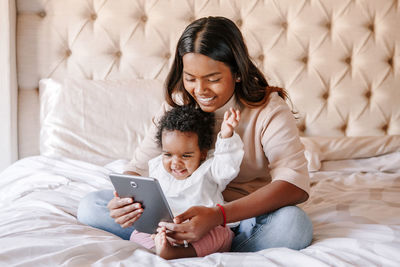 Mixed race indian black mother with toddler baby girl watching cartoons on tablet. ethnic diversity. 