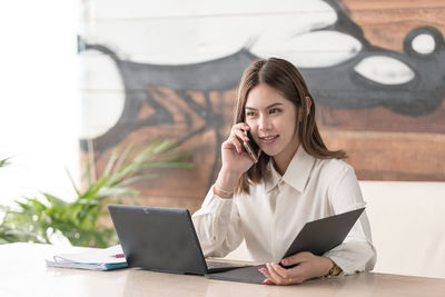 Young woman using mobile phone while sitting on table