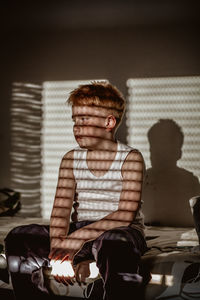 Boy looking away while sitting on bed at home