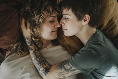 Directly above shot of lesbian couple rubbing noses while lying down on bed with eyes closed at home