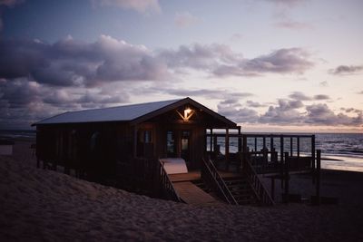 Built structure on beach by sea against sky during sunset