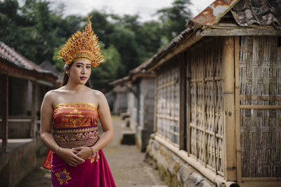 Portrait of young woman wearing traditional clothing standing on road amidst huts