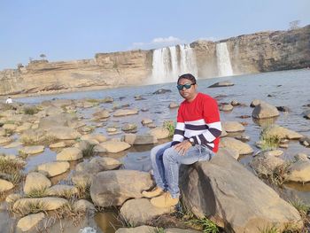 Full length portrait of young man standing on rock against sky