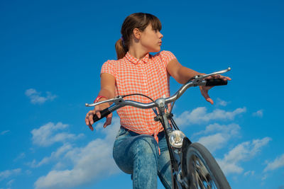 Low angle view of woman riding bicycle against blue sky