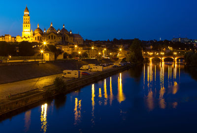 Illuminated buildings by river against sky at night