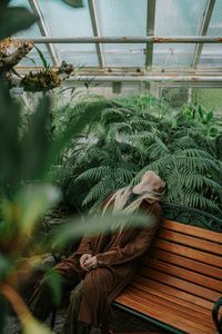 Young woman sitting on bench against plants