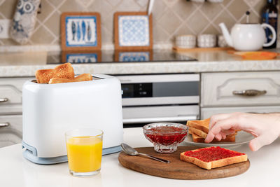 Male hand reaches for a crunchy toast with raspberry jam. white toaster, glass of orange juice