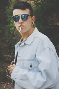 Portrait of young man holding cigarette in mouth while standing outdoors