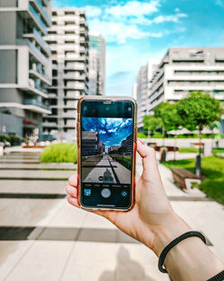 Hand holding mobile phone against buildings in city
