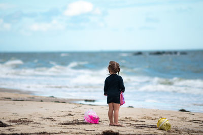 Rear view of boy standing at beach against sky