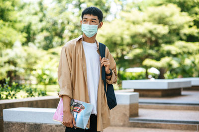 Portrait of young man holding camera while standing outdoors