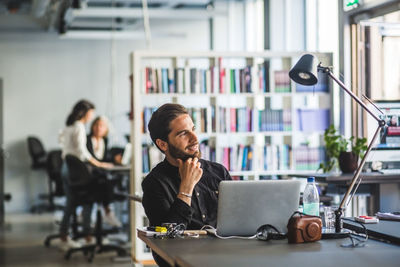 Confident businessman looking away while sitting at desk in office