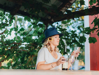 Portrait of woman holding hat against plants